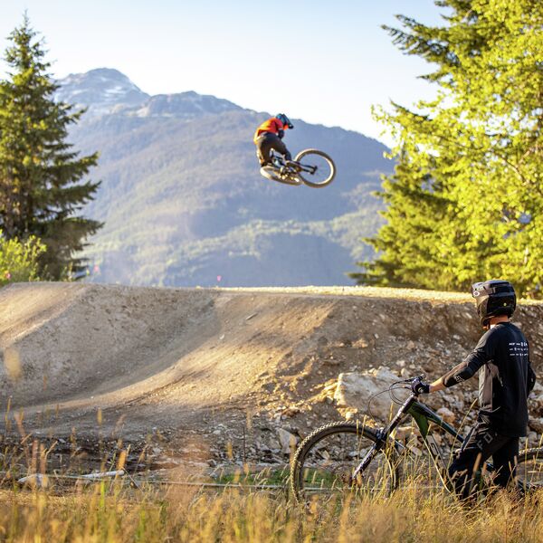 Bike School Coach watches rider whip bike on jump 